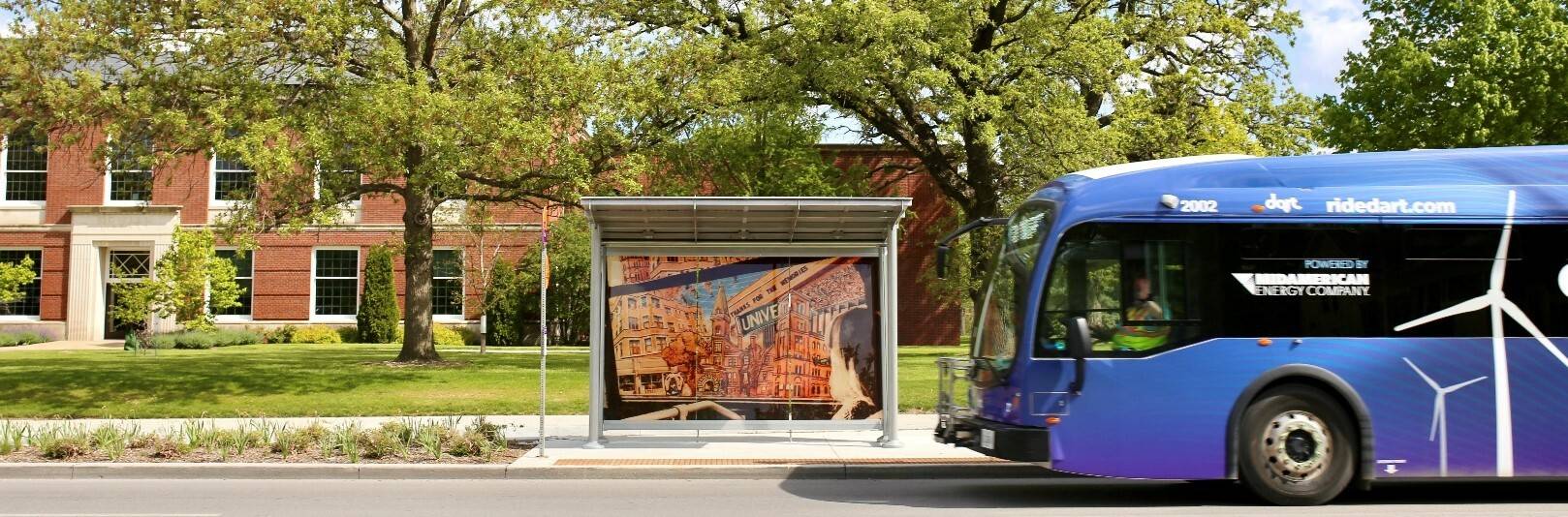 An electric bus passes an art bus shelter at Drake University.